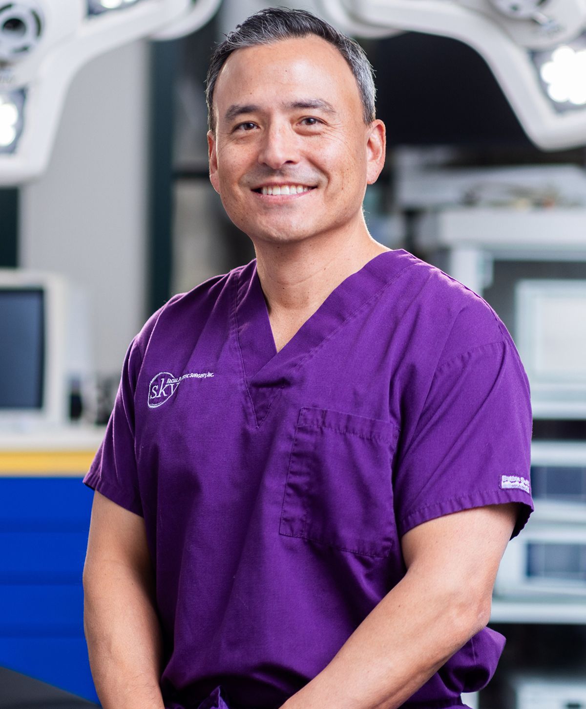 Smiling man in purple scrubs, medical environment.