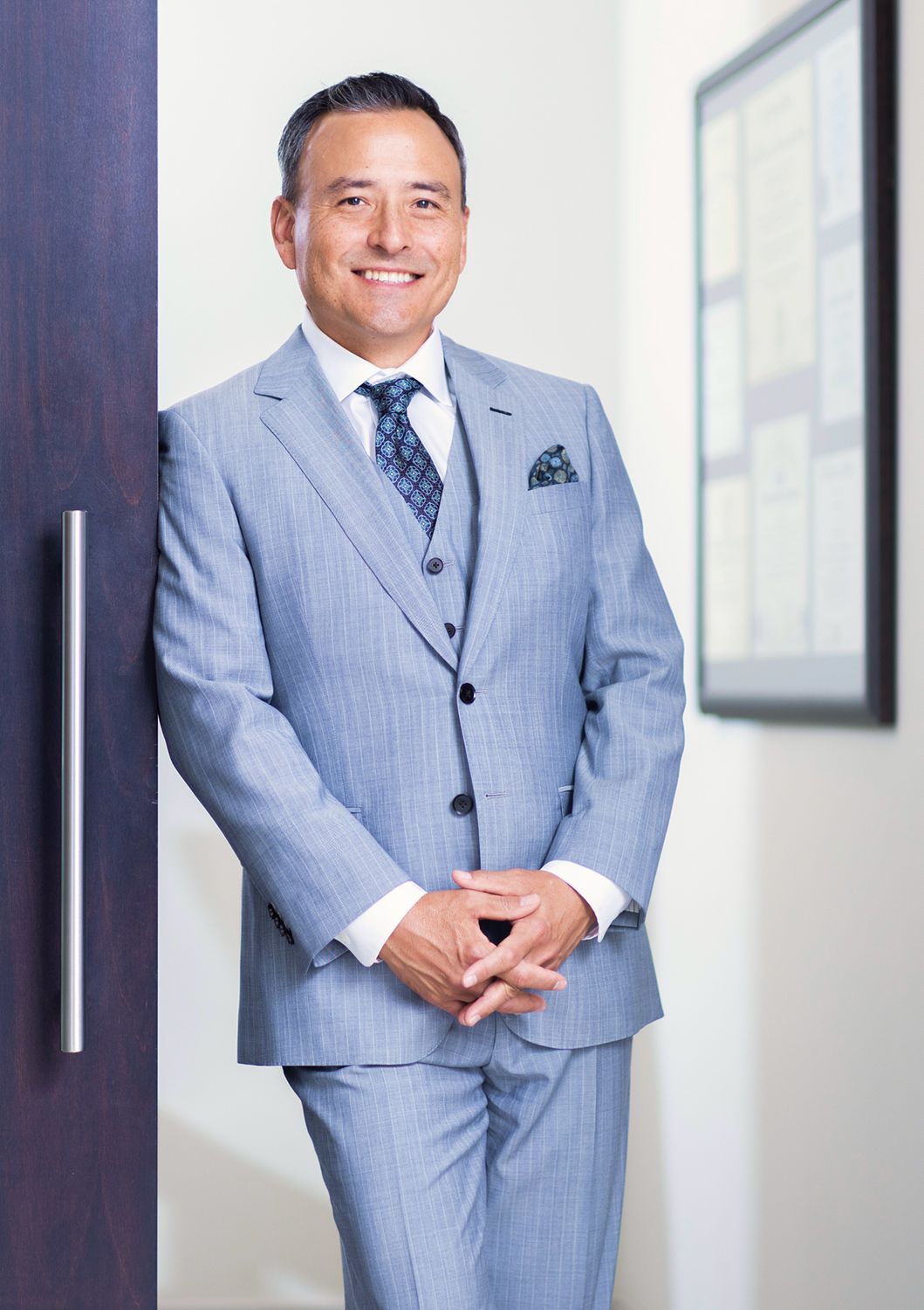 Smiling man in gray suit standing by door.