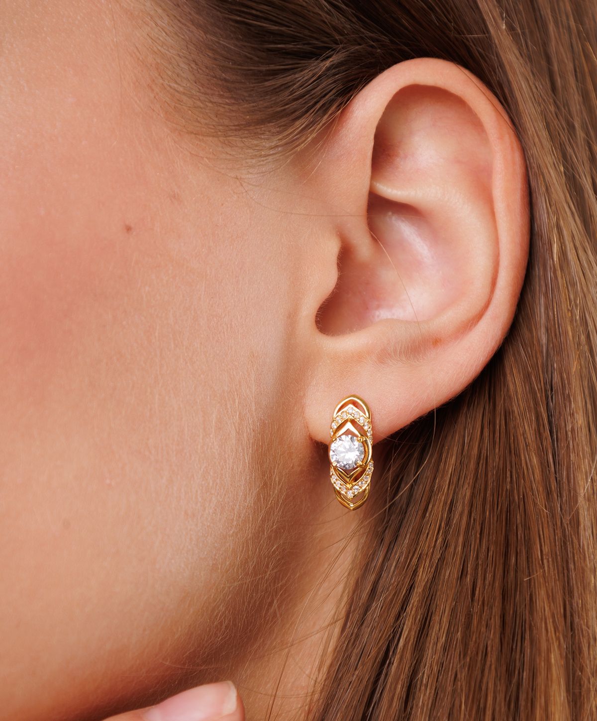 Gold earrings worn on a woman's ear.